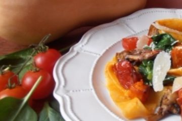 An image showing 2 Method Pasta with Squash, Mushrooms and Spinach on a white patterned plate on a wooden surface, surrounded by a whole squash, spinach, cherry tomatoes, and mushrooms, with a purple background.