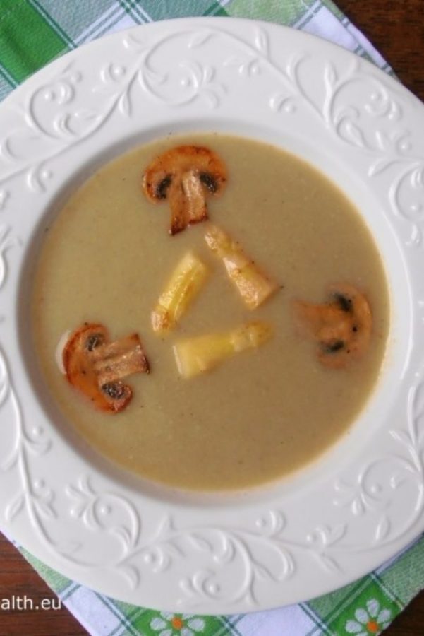 An image showing Asparagus and Mushroom Soup in a white patterned bowl on a checkered towel on a wooden surface.