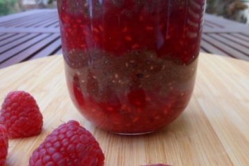 An image of a glass with layers of chocolate chia pudding and raspberry mousse with a few raspberries next to it.