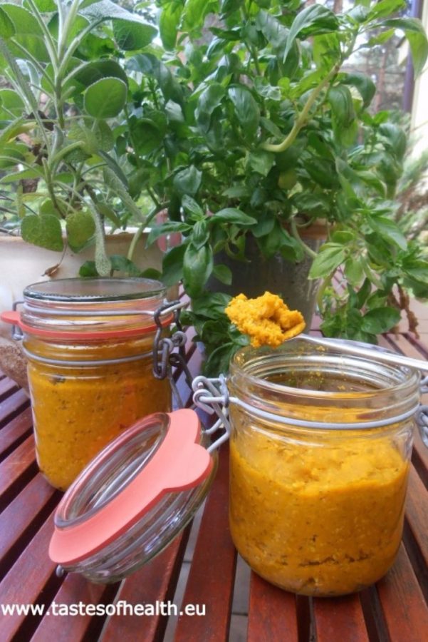 An image showing two jars of Concentrated Vegetable Stock Paste, with one jar open and with a teaspoon full of the paste on top of the jar- both jars are on a wooden table and have greenery behind them.