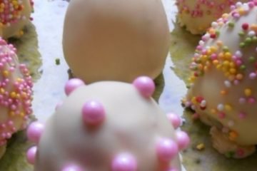 An image showing a number of cookie dough Easter eggs, covered in white chocolate and sprinkles, on a kiwi-pattered plate on a wooden floor.