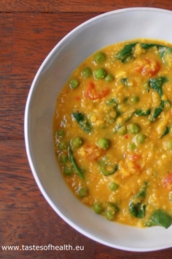 An image showing Dhal with Spinach and Green Peas in a white bowl, on a wooden surface.