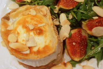An image showing Grilled Goat's Cheese and Fig Salad with rocket and toasted almonds on a white plate on a marbled surface.