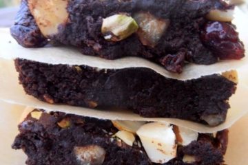An image showing Healthy Avocado Brownies, with the pieces stacked on top of each other, with baking paper separating them, with greenery as the background.