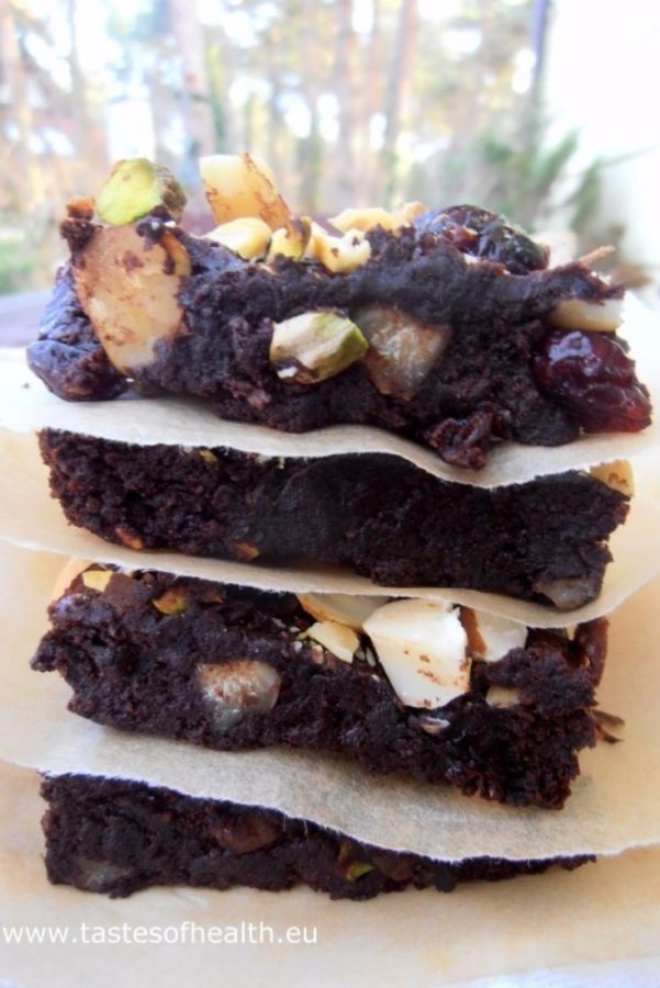 An image showing Healthy Avocado Brownies, with the pieces stacked on top of each other, with baking paper separating them, with greenery as the background.