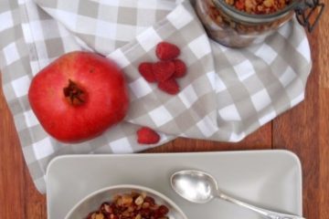 An image of Homemade Granola with Red Berries (strawberries, raspberries) in a jar and also served in a bowl with yogurt and pomegranate seeds.