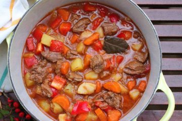 An image showing Hungarian Goulash in a white bowl, with the peppers, potatoes, and meat clearly visible.