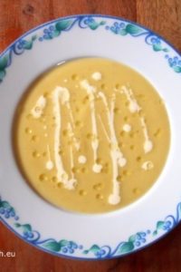 An image showing Leek and Potato Soup with Truffle Oil in a white bowl with blue flowers on the edges on a wooden surface.