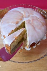An image showing Lemon Cake with Chia Seeds on a glass plate on a wooden surface with a pink background.