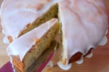 An image showing Lemon Cake with Chia Seeds on a glass plate on a wooden surface with a pink background.