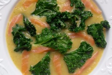 An image showing Lemony Soup with Kale and smoked salmon in a white patterned bowl on a wooden surface.
