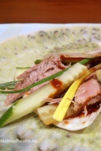 An image showing pieces of Peking duck, cucumber, hoisin sauce, spring onion, and a pancake on a light green plate.