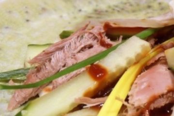 An image showing pieces of Peking duck, cucumber, hoisin sauce, spring onion, and a pancake on a light green plate.
