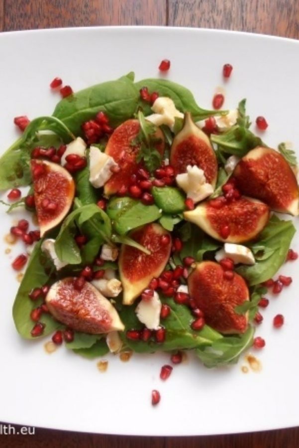 An image showing a Salad with Figs, Pomegranate and Goat's Cheese on a white square plate on a wooden surface.