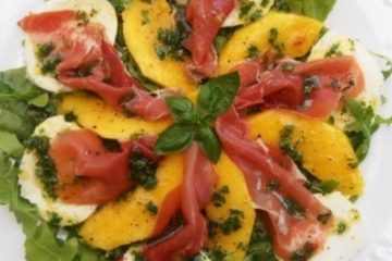 An image of a salad with prosciutto, mozzarella, mango and rocket on a white plate.