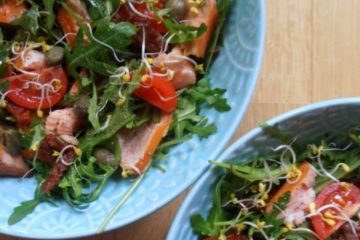 An image of a Smoked Salmon and Tomato Salad, split between two blue bowls, on a wooden surface.