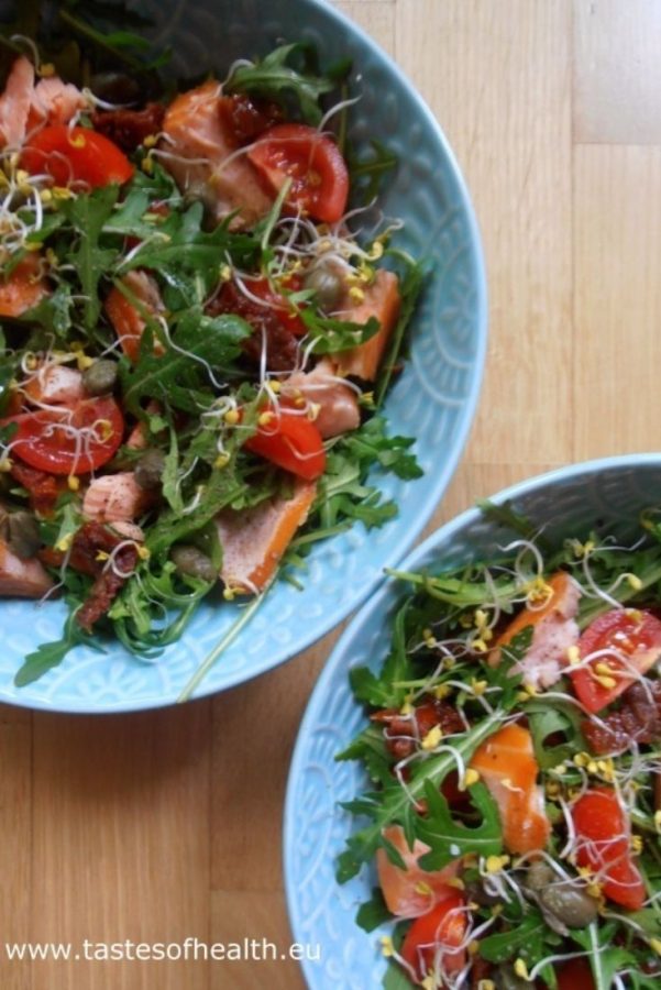 An image of a Smoked Salmon and Tomato Salad, split between two blue bowls, on a wooden surface.