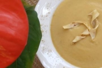 An image of a spicy parsnip soup in a white plate, on a wicker table, with a red plant with green leaves next to it.