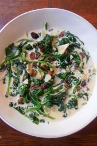 An image of spinach with raisins, garlic, onion, cream, and honey, served on a white plate.