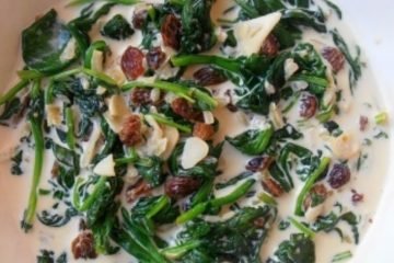 An image of spinach with raisins, garlic, onion, cream, and honey, served on a white plate.