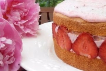An image of Sponge Cake with Strawberry Mousse on a white plate with pink peonies next to it.