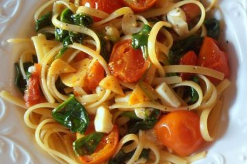 An image showing Spaghetti with Spinach, Mozzarella and Tomatoes on a white patterned plate on a marbled surface.