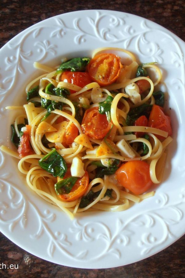 An image showing Spaghetti with Spinach, Mozzarella and Tomatoes on a white patterned plate on a marbled surface.