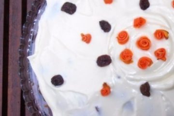 An image of a Healthier carrot Cake with white icing and orange and brown decoration on top.