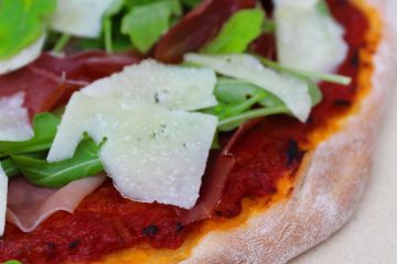 An image of Prosciutto Arugula Pizza on a light beige stone.