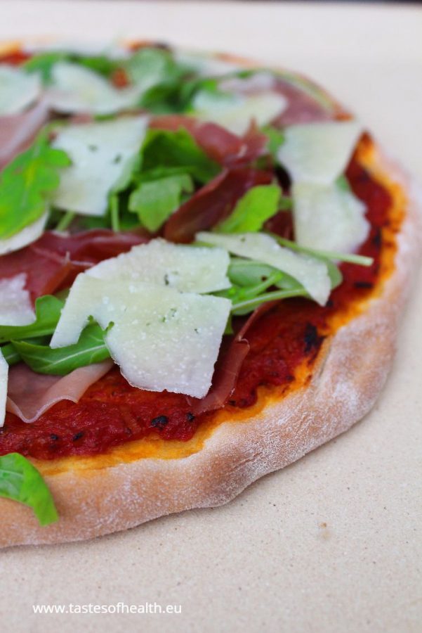 An image of Prosciutto Arugula Pizza on a light beige stone.