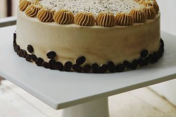 An image of Coffee Almond Cake on a white dish. The cake is decorated with coffee beans and cofee cream on top.