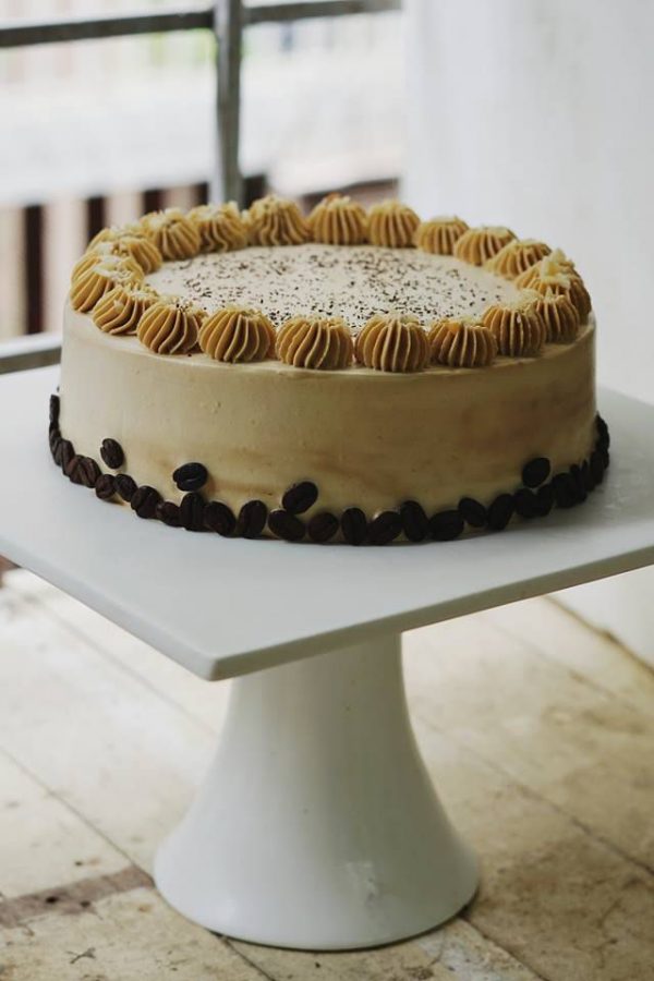 An image of Coffee Almond Cake on a white dish. The cake is decorated with coffee beans and cofee cream on top.