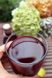 An image of Fermented Beet Kvass in a glass. There are blooms in the background.