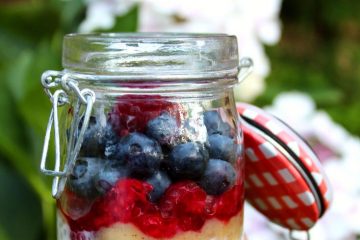 Banana Tapioca Pudding (no sugar desserts) topped with raspberries and blueberries seen from a side. There is a white bloom in the background.