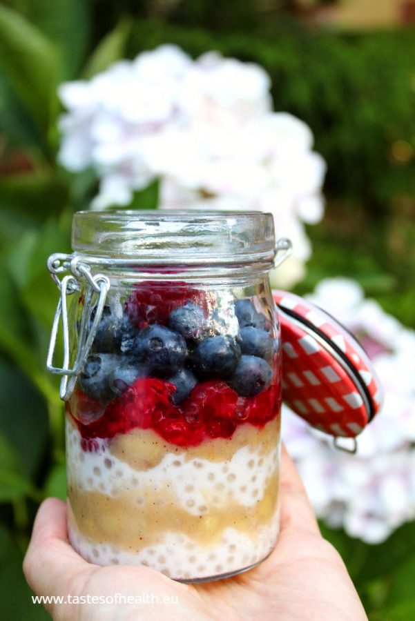 Banana Tapioca Pudding (no sugar desserts) topped with raspberries and blueberries seen from a side. There is a white bloom in the background.