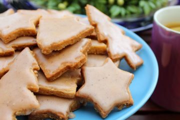 An Image of Gingerbread Cookies Gluten Free on a blue plate. There is a pink mug with tea and lemon and green wreath next to it.