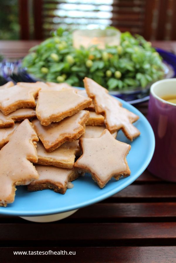 An Image of Gingerbread Cookies Gluten Free on a blue plate. There is a pink mug with tea and lemon and green wreath next to it.