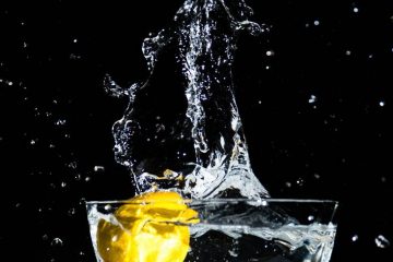 Benefits of Drinking Water with Lemon Juice. An image of a lemon falling into a bowl of water and splashing it.