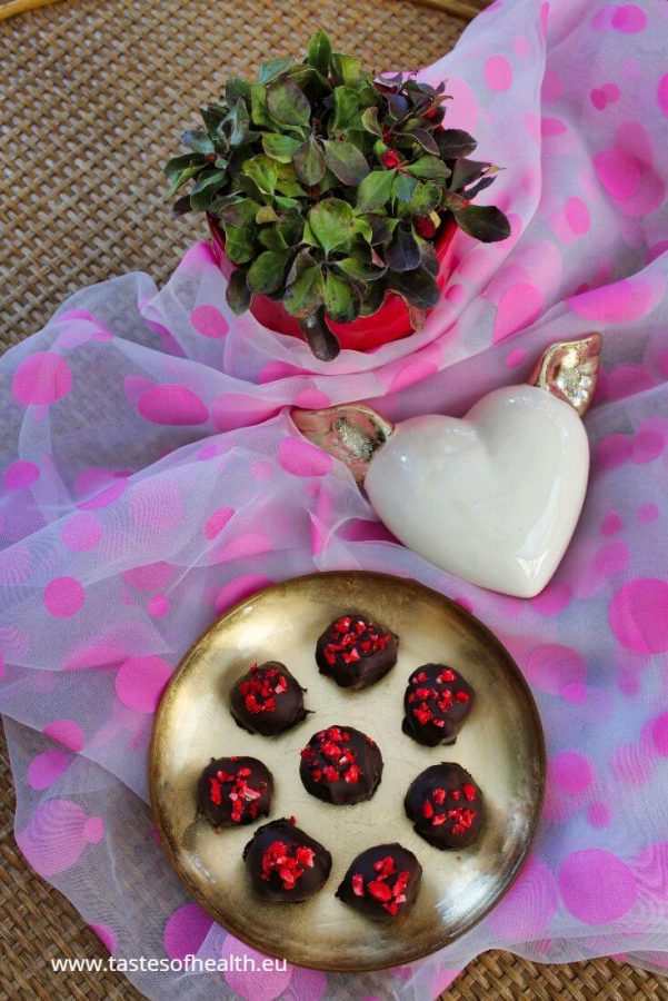 Strawberry Cheesecake Bites - homemade pralines recipes. Homemade chocolates are presented on a golden plate. There is a white heart with golden wings and a red flower pot with a green plant next to it.