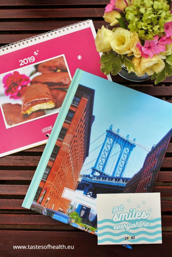 A picture taken from above of a pink calendar, a photobook with holiday pictures and a cream and pink flower arrangement.