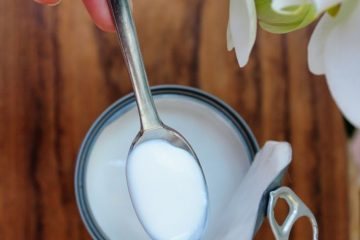 An image of Vegan Heavy Cream Substitutes: coconut cream on a spoon and in a can standing on a wooden surfice. There is also a white orchid next to it.