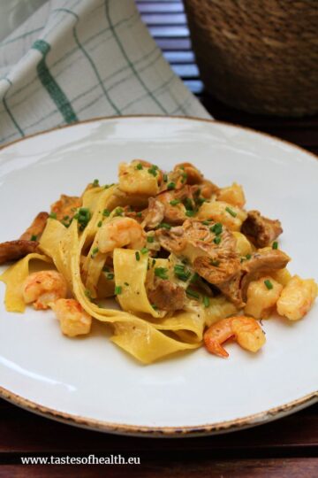 A close up of Pasta with Chanterelles, Prawns and Saffron Sauce on a white plate.